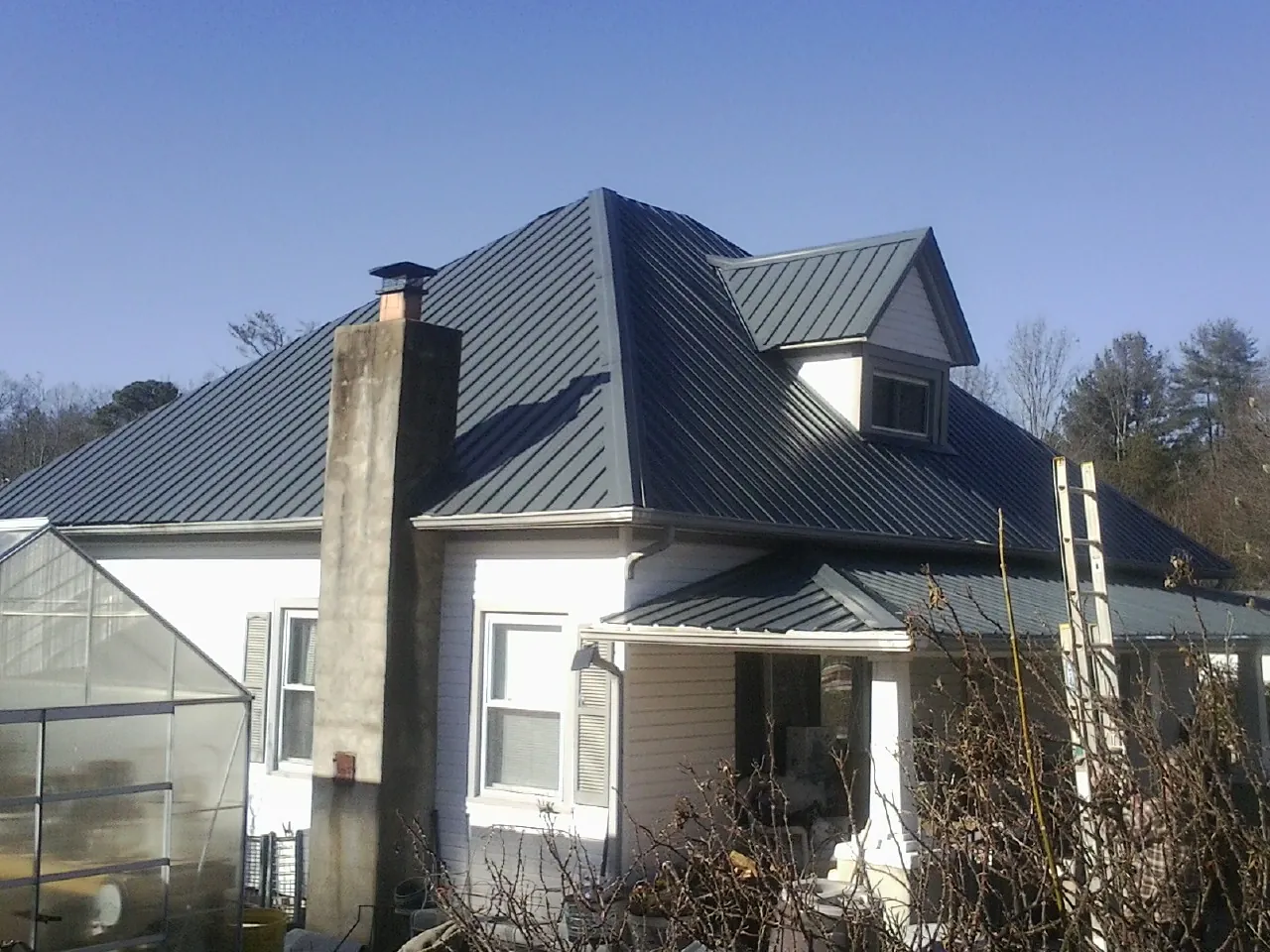 Dark blue standing seam metal roof on a white farmhouse with dormer — Slate & Tile Roof Repair by Roofing Brothers in Buckland