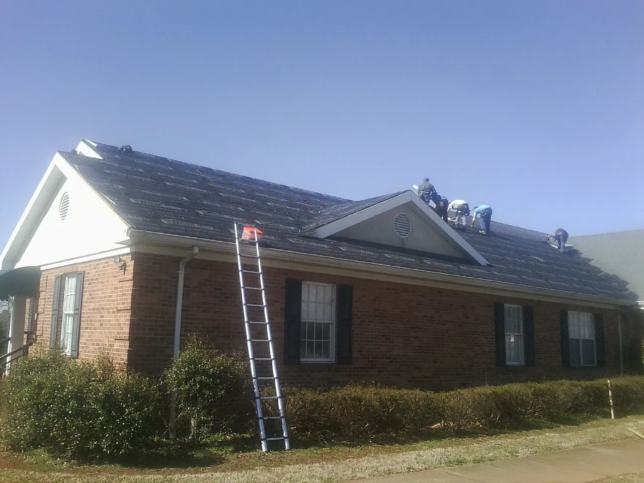 Crew tearing shingles off a brick ranch roof with a ladder set — Emergency Roof Repair work by our crew in Buckland