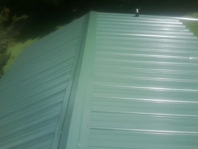 New green metal panels meeting at the ridge of a roof — Flat Roof Repair work by our crew in Buckland