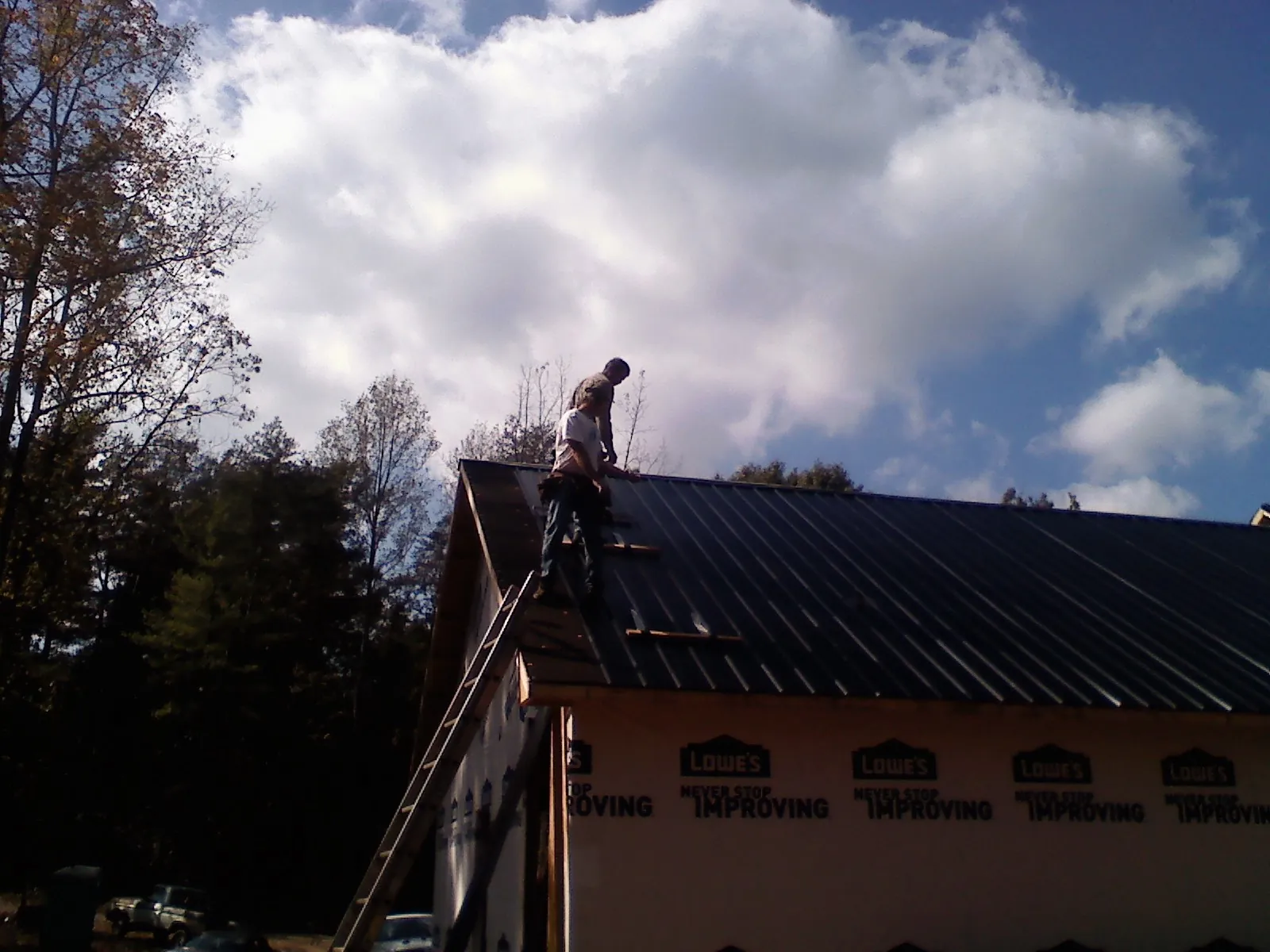 Roofer fastening dark metal panels high against a cloudy sky, from a Roof Inspection job in Buckland